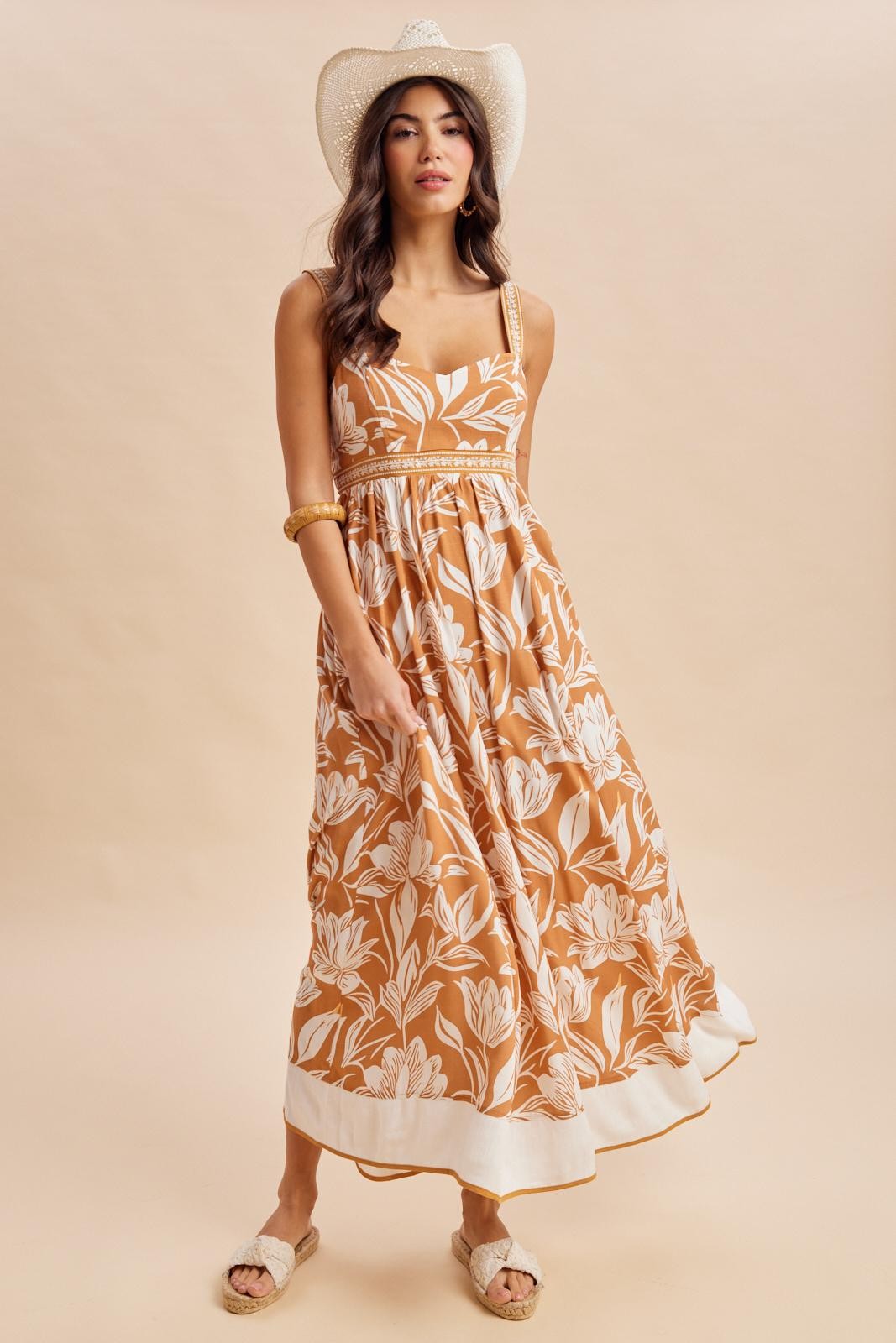 woman wearing a brown floral maxi dress with spaghetti straps and a tiered skirt, styled with a wide-brimmed hat
