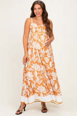 woman wearing an orange floral print maternity maxi dress and gently cradling her baby bump