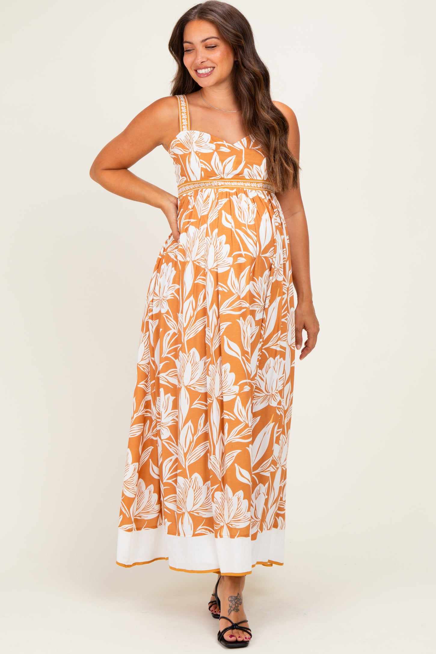 woman wearing an orange floral print maternity maxi dress with a fitted empire waist and flowy skirt, showing her baby bump