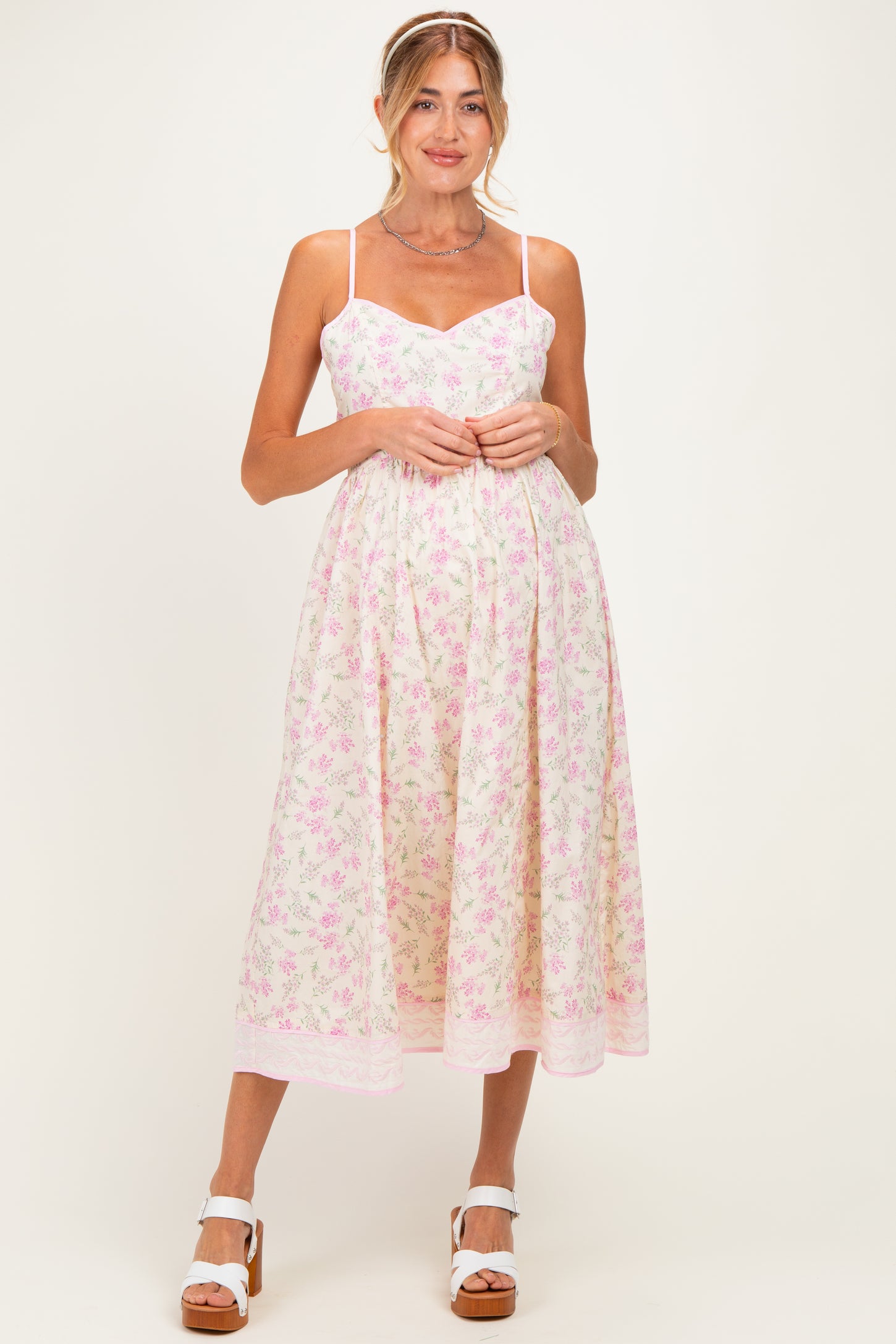 woman wearing a pastel floral print maternity dress with a sweetheart neckline and adjustable straps