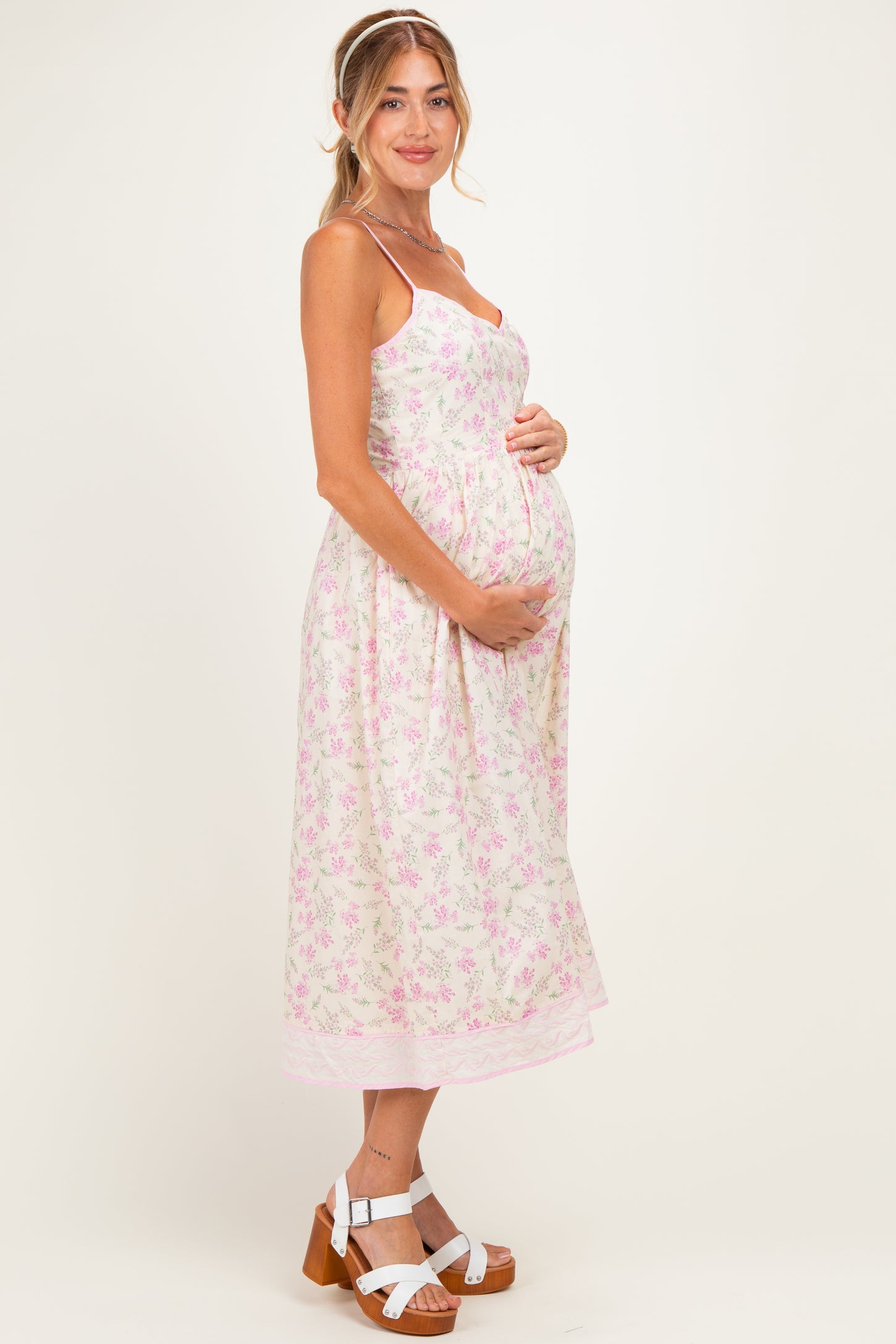 woman wearing a floral light pink maternity dress and holding her baby bump