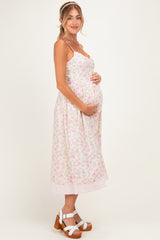 woman wearing a floral light pink maternity dress and holding her baby bump