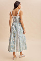 woman wearing a blue and white floral maxi dress with a smocked back and wide straps, seen from the back