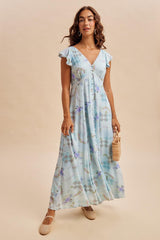 woman wearing a light blue floral maxi dress with flutter sleeves, posing with a small handbag