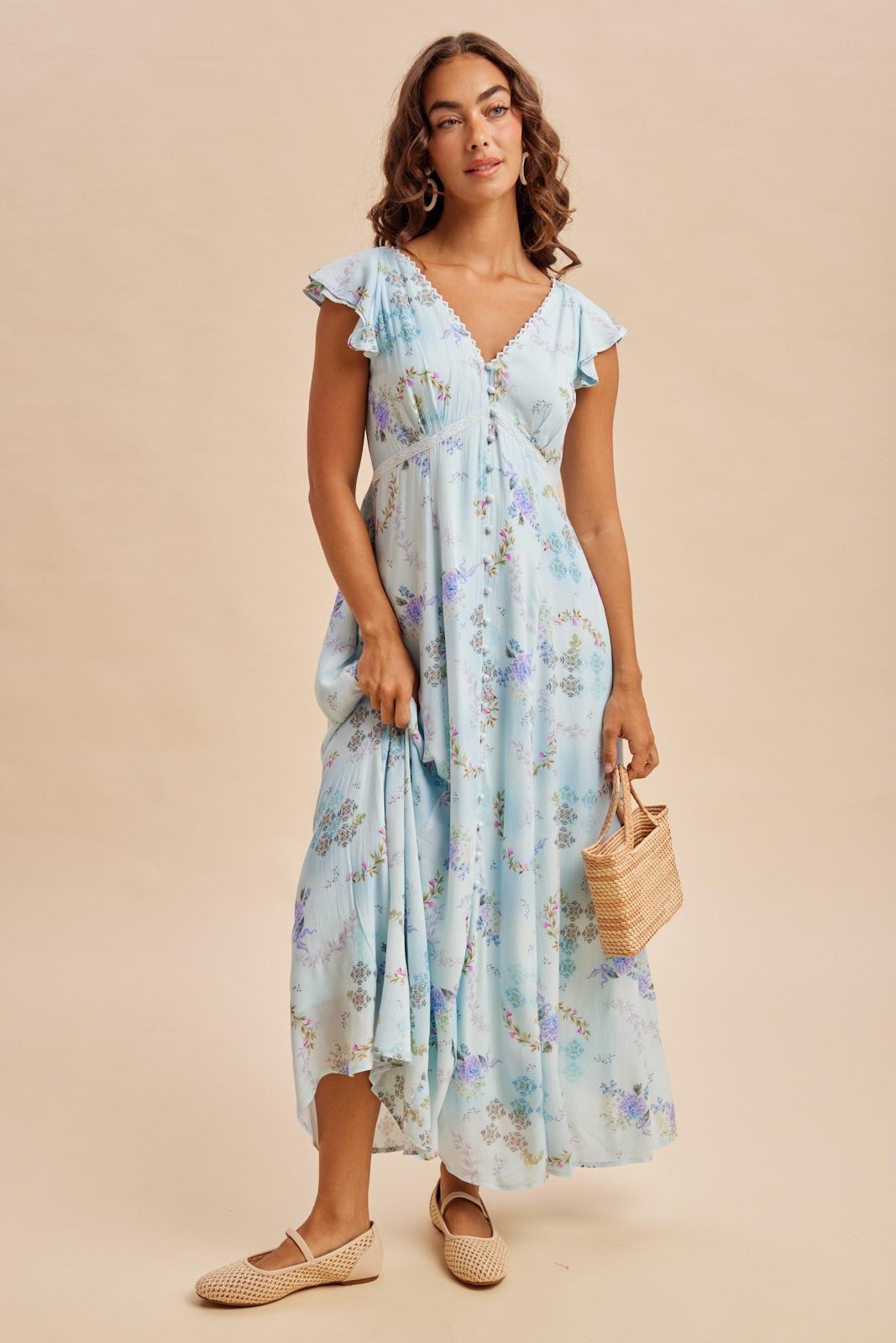 woman wearing a light blue floral maxi dress with flutter sleeves and holding a straw bag