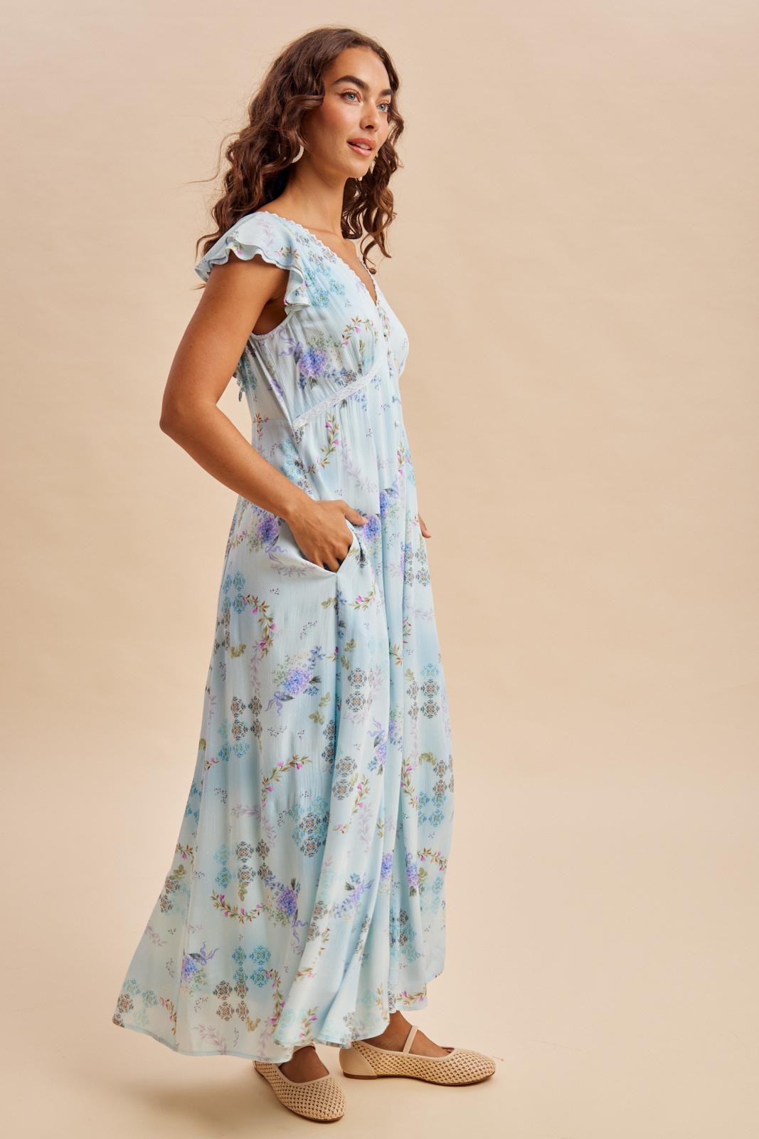 woman wearing a light blue floral maxi dress with ruffle sleeves and pockets, styled with casual woven shoes