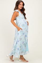 woman wearing a light blue floral maternity maxi dress with ruffle sleeves and pockets, gently cradling her baby bump