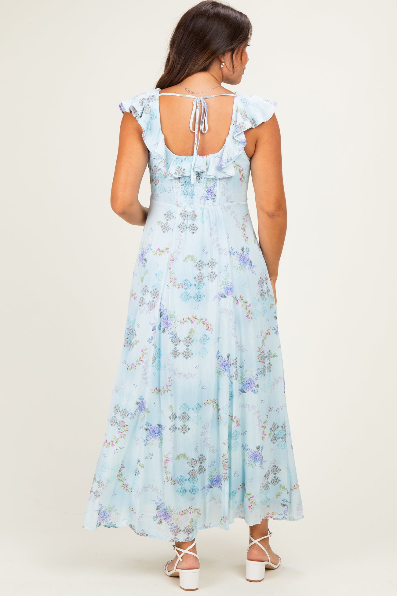 woman wearing a light blue floral maternity maxi dress with ruffle sleeves and a tie back detail