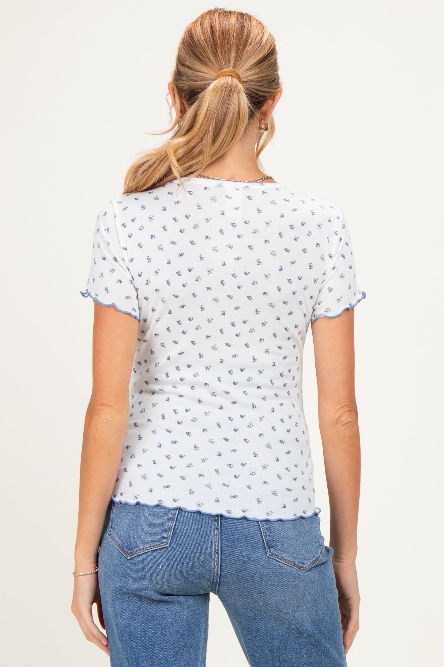 woman wearing a short sleeve white maternity top with blue floral patterns and scalloped edges, showing her back