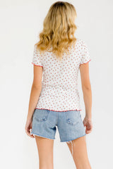 woman wearing a white short sleeve top with pink floral print and frayed denim shorts, viewed from the back