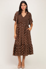 woman wearing a brown polka dot midi dress with a v-neck and short sleeves, standing with hands in pockets