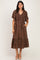 woman wearing a brown polka dot midi dress with a v-neck and short sleeves, standing with hands in pockets