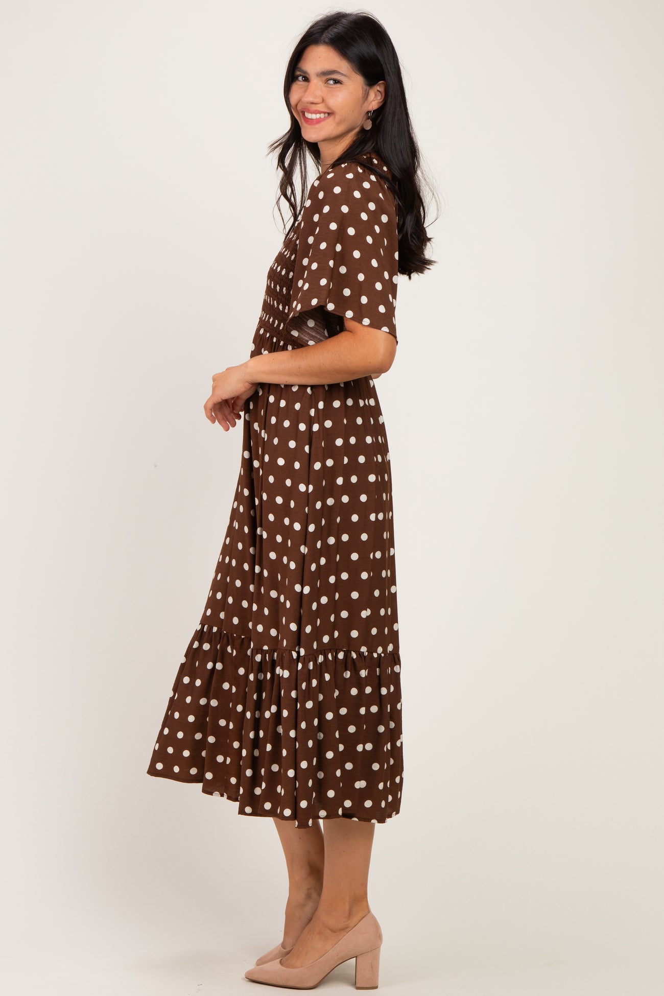 woman wearing a brown polka dot midi dress with a tiered skirt and short sleeves, standing in profile