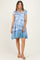 woman wearing a blue floral print maternity dress with ruffled sleeves and a tiered skirt, standing and smiling