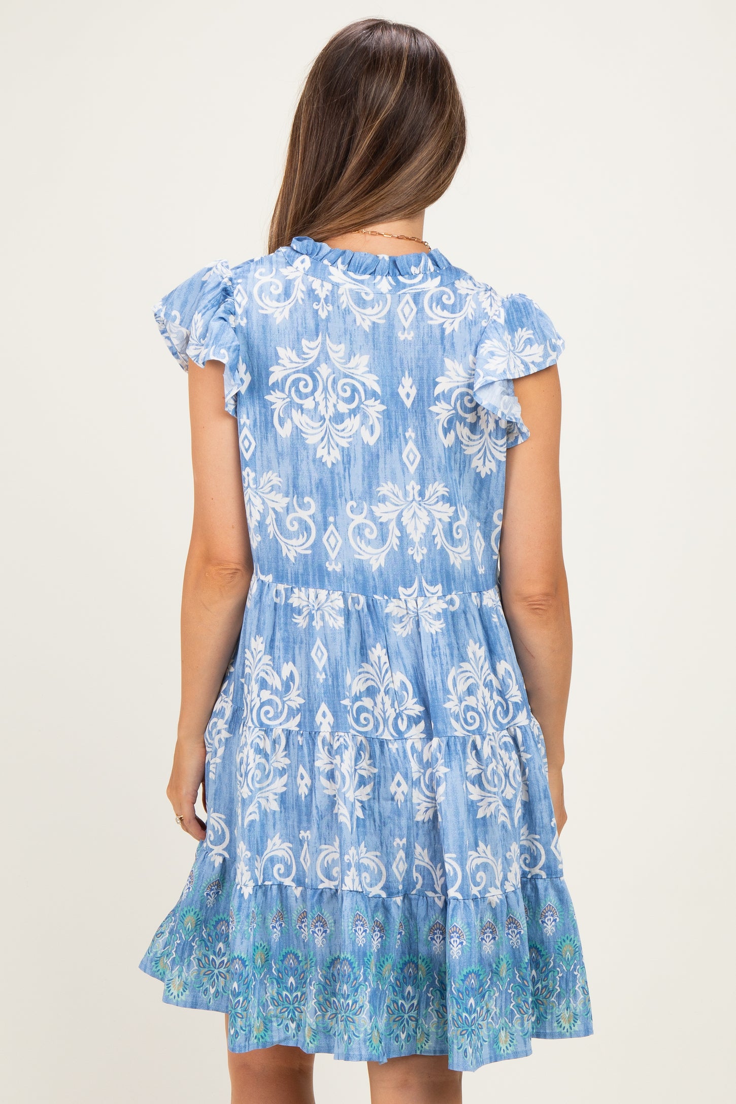 woman wearing a blue floral patterned maternity dress with ruffled sleeves and a tiered skirt from the back