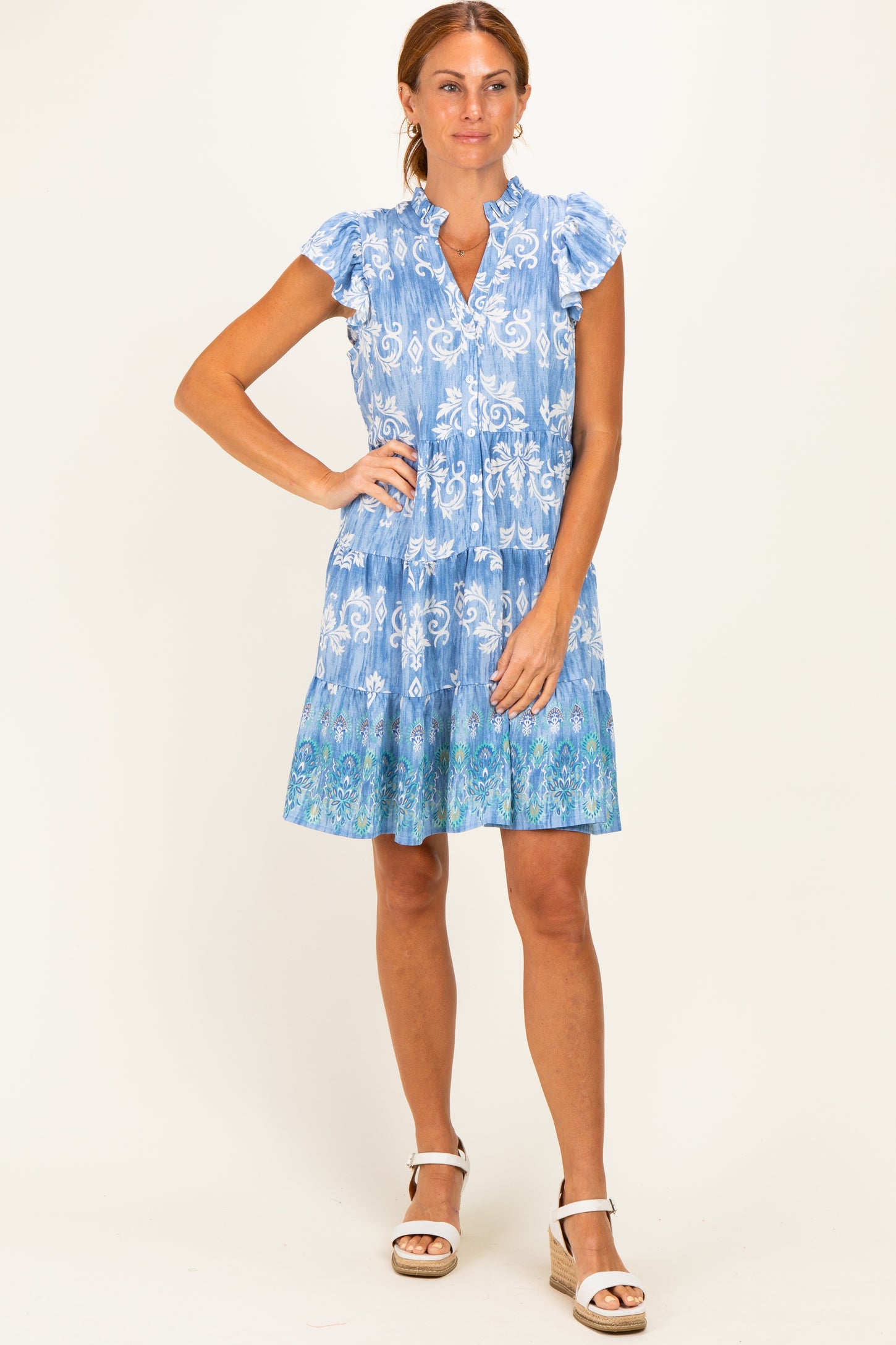 woman wearing a blue floral short sleeve dress with ruffled sleeves and a tiered skirt, standing on a neutral background