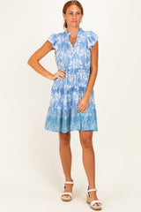 woman wearing a blue floral short sleeve dress with ruffled sleeves and a tiered skirt, standing on a neutral background