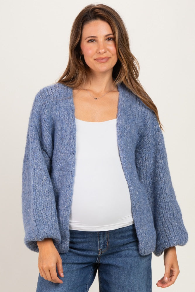 woman wearing a light blue chunky-knit maternity cardigan over a white top, showing her baby bump