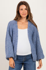 woman wearing a light blue chunky-knit maternity cardigan over a white top, showing her baby bump