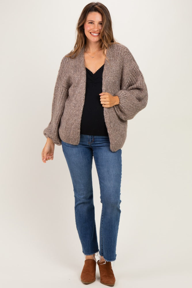 woman wearing a cozy taupe maternity cardigan over a black top with jeans, smiling and posing casually