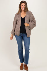 woman wearing a cozy taupe maternity cardigan over a black top with jeans, smiling and posing casually