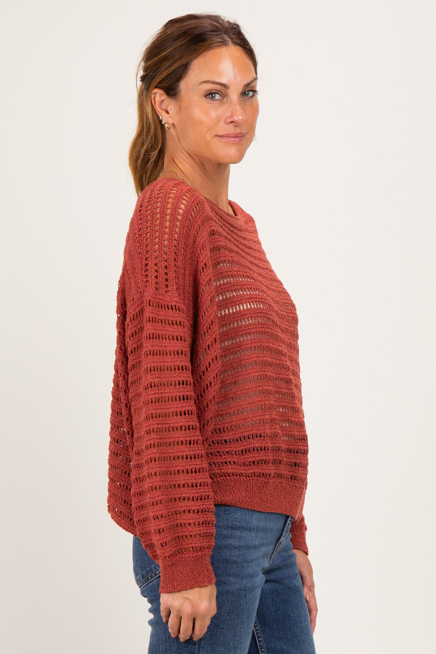 woman wearing a rust-colored open knit sweater with a relaxed fit and long sleeves, paired with blue jeans