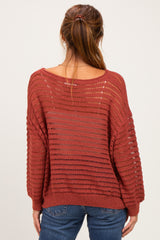 woman wearing a rust-colored loose-knit sweater with a wide neckline and long sleeves, viewed from the back