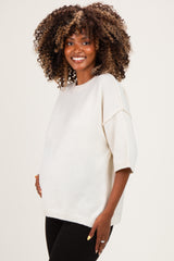 woman wearing a cream oversized maternity sweater with short sleeves and a visible baby bump