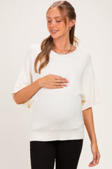 woman wearing a cream short sleeve maternity sweater and cradling her baby bump