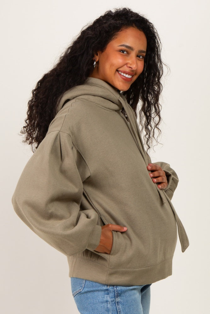 woman wearing a light olive green maternity hoodie with a front zipper and large sleeves, showing a baby bump