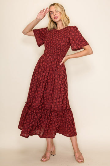 woman wearing a burgundy floral maxi dress with smocked bodice and ruffled hemline, posing with one hand raised