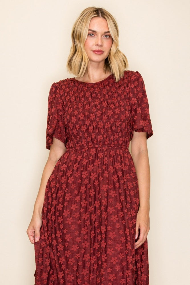 woman wearing a burgundy floral print short sleeve dress with smocked detailing at the bodice