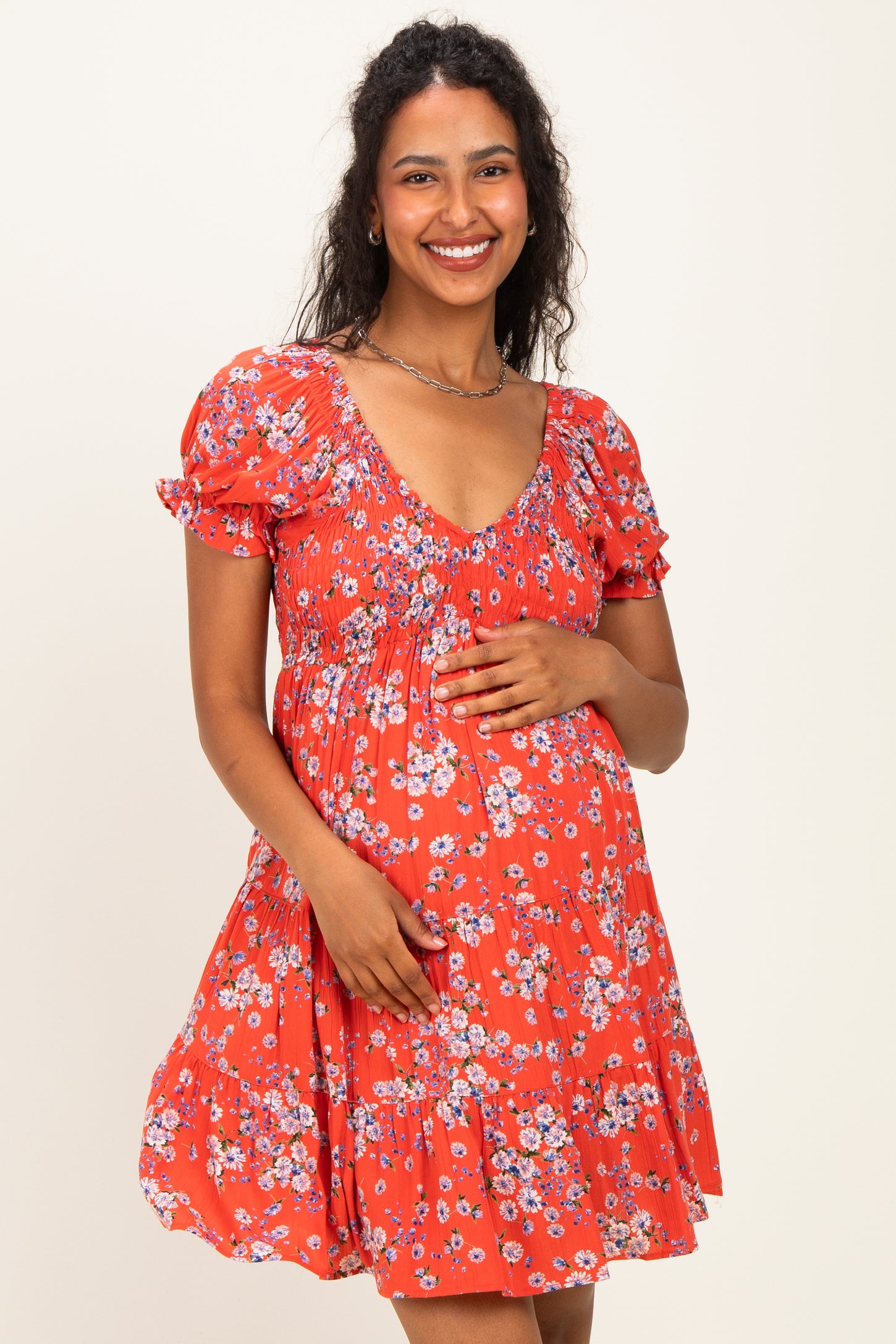 woman wearing a red floral maternity dress with short puff sleeves and a fitted bodice, holding her baby bump