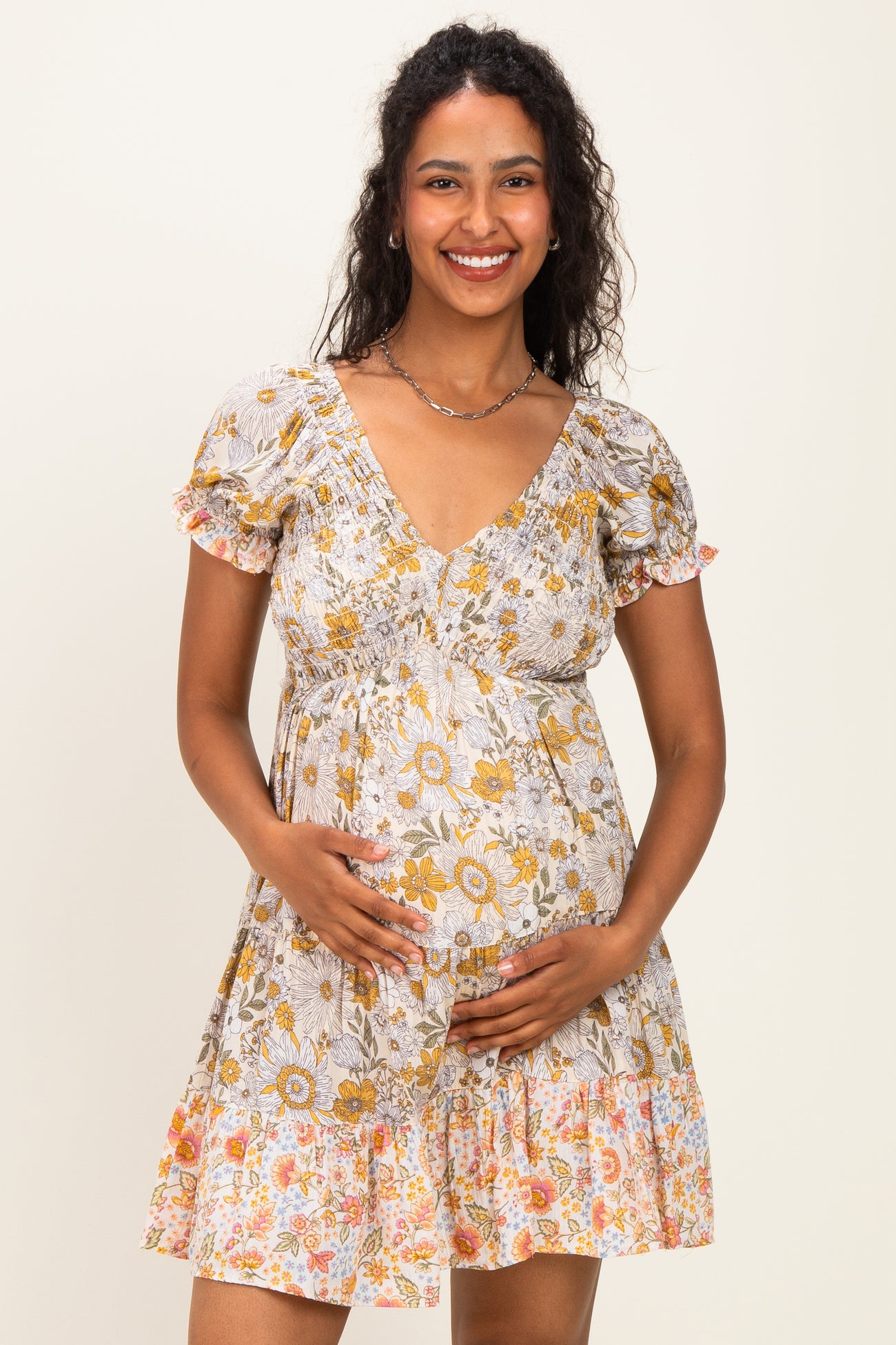 woman wearing a floral print maternity dress with short puff sleeves and a gathered waist, holding her baby bump