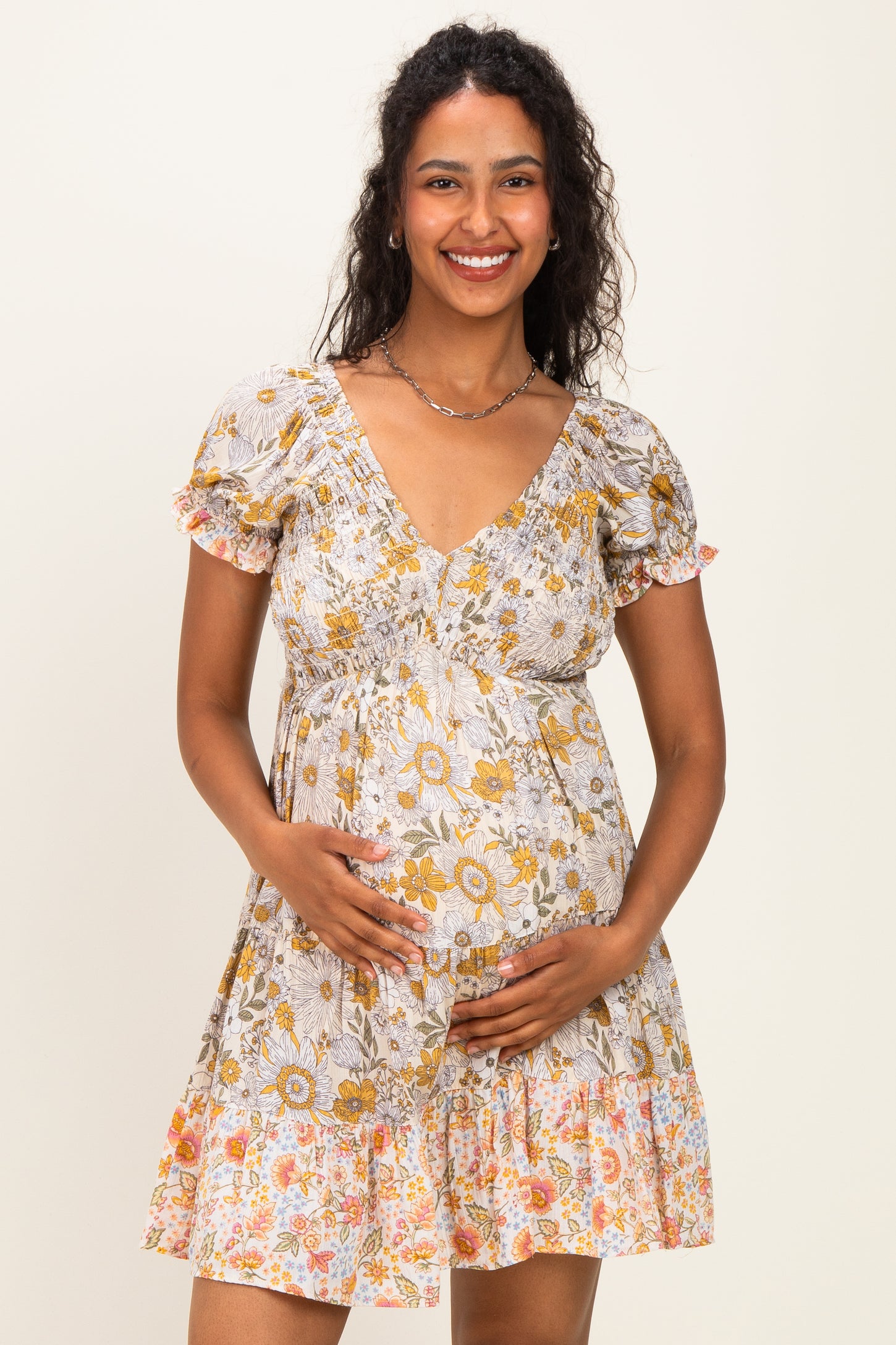 woman wearing a floral print maternity dress with short puff sleeves and a gathered waist, holding her baby bump