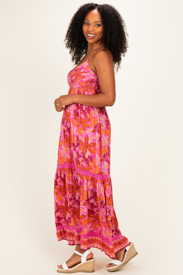 woman wearing a pink floral maxi dress with a tiered skirt and spaghetti straps, standing sideways with curly hair