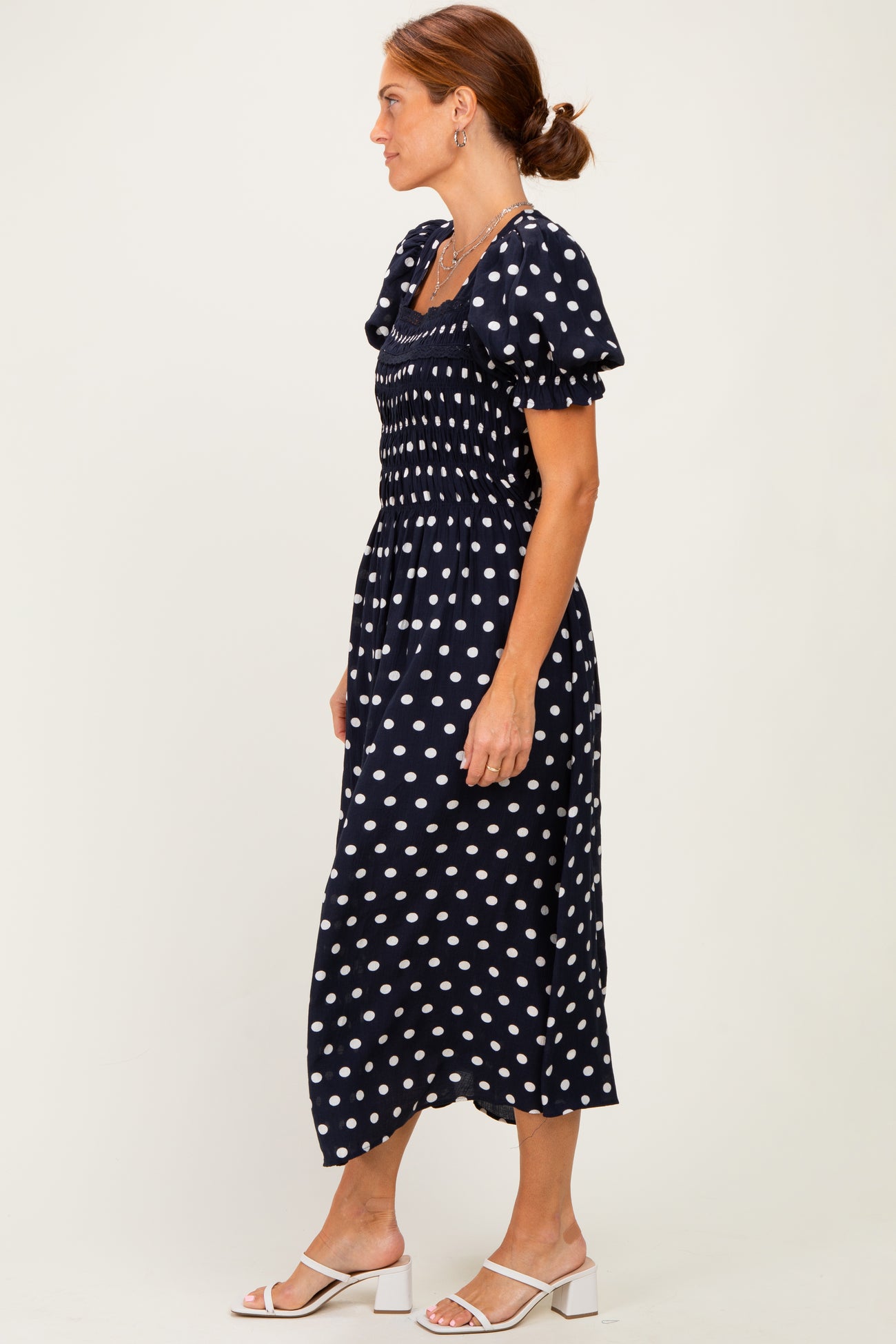 woman wearing a navy blue polka dot midi dress with puff sleeves and a smocked bodice