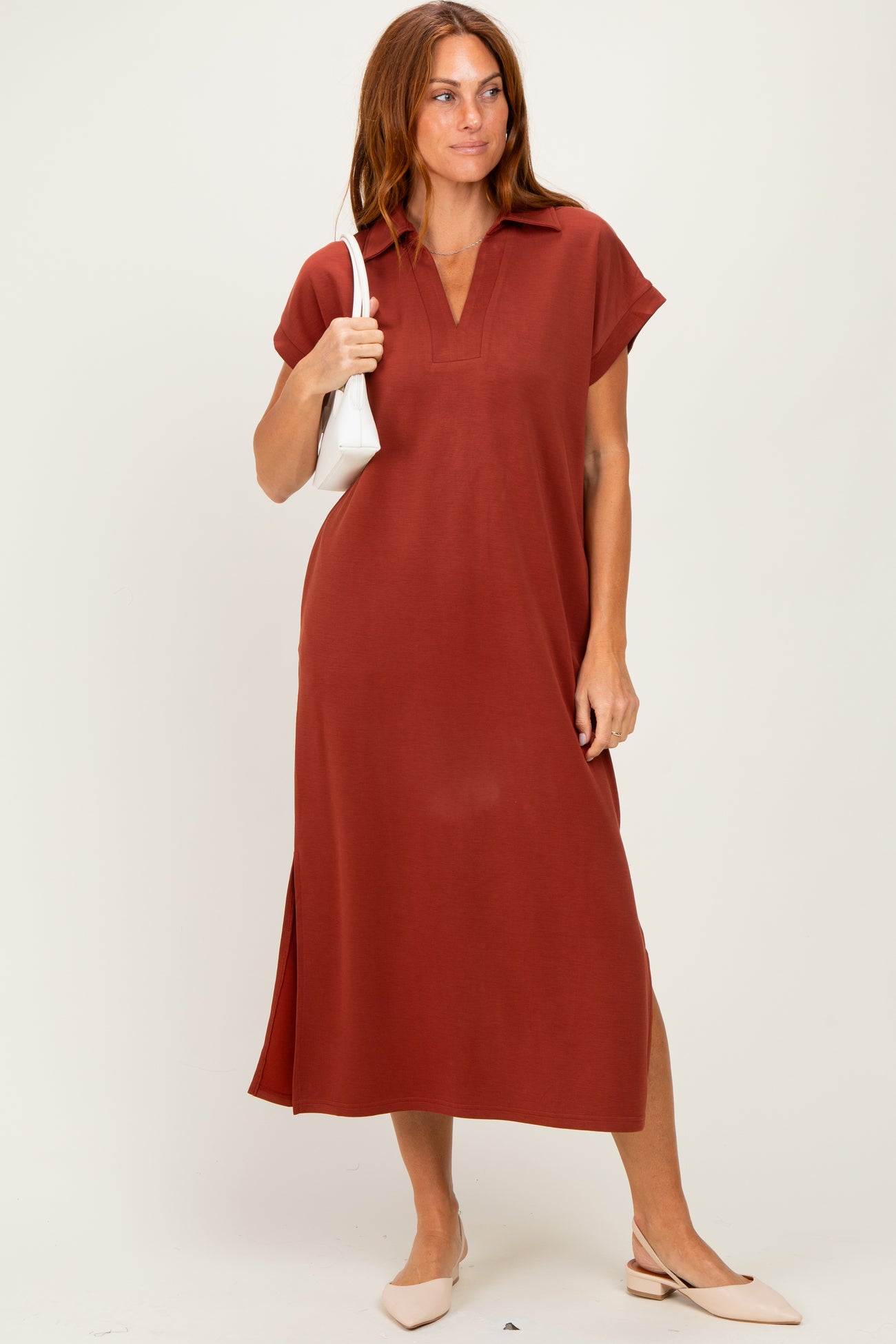 woman wearing a rust-colored short sleeve midi dress with a collar and side slits, holding a white handbag