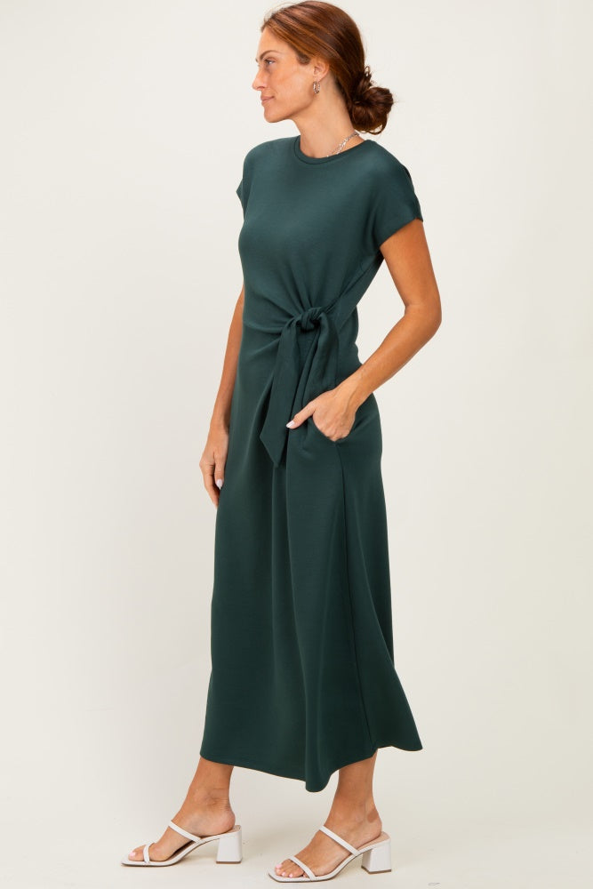 woman wearing a dark green short sleeve maxi dress with a tie waist and white block heel sandals