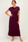 woman wearing a burgundy maxi dress with short sleeves and a knot detail at the waist, posing with one hand on her hip