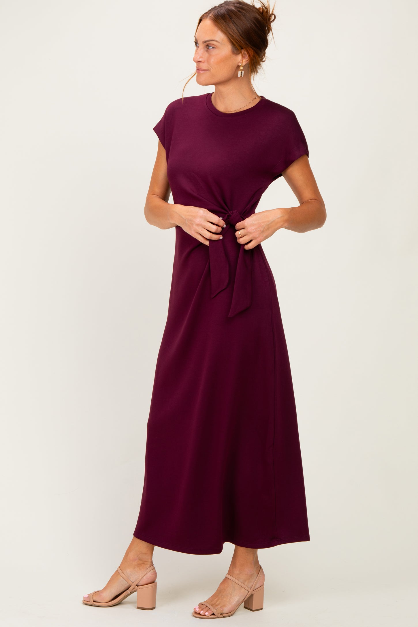 woman wearing a burgundy cap sleeve maxi dress with a tie waist detail and beige block heel sandals