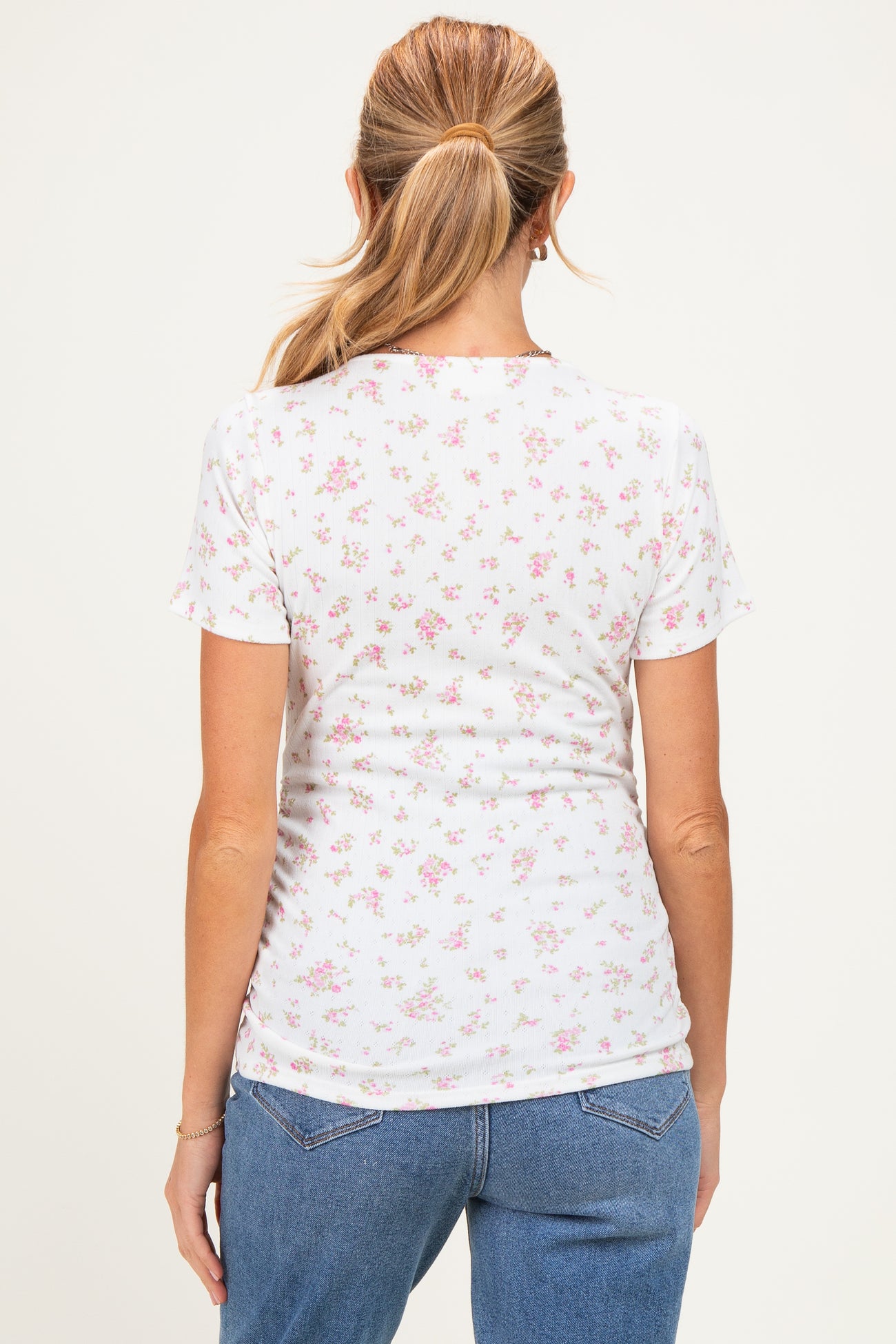 woman wearing a floral print white maternity top, view from the back with short sleeves and a fitted style