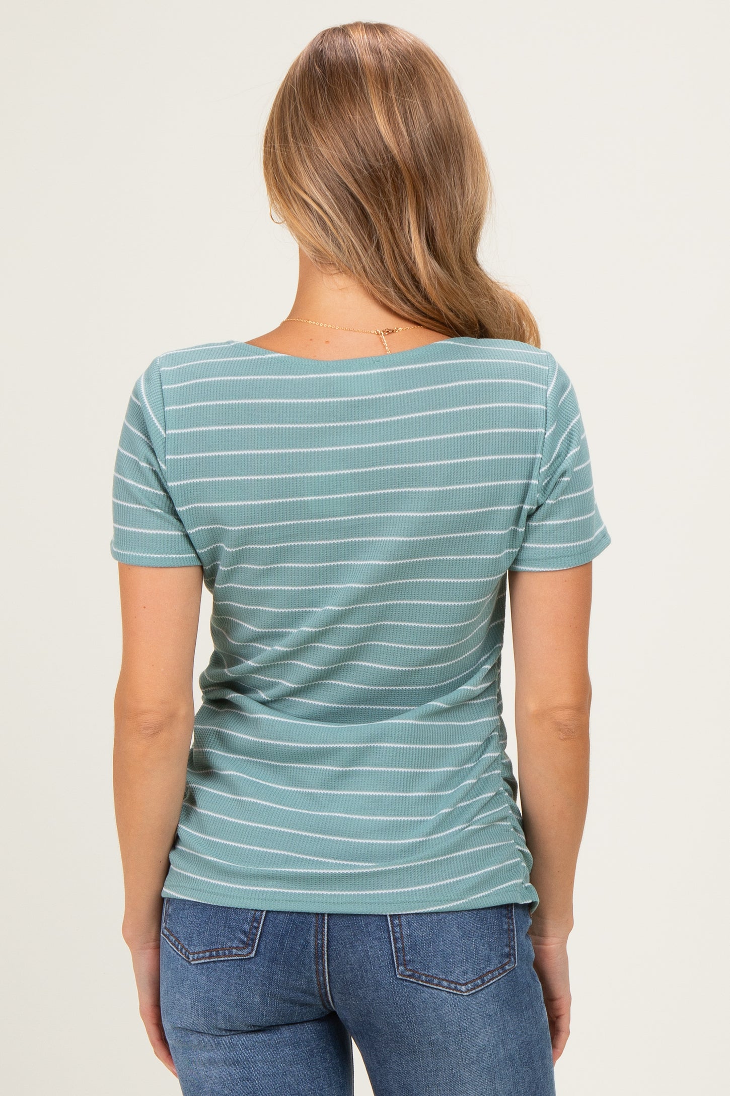woman wearing a teal striped short sleeve top with a fitted silhouette and ruching detail on the sides