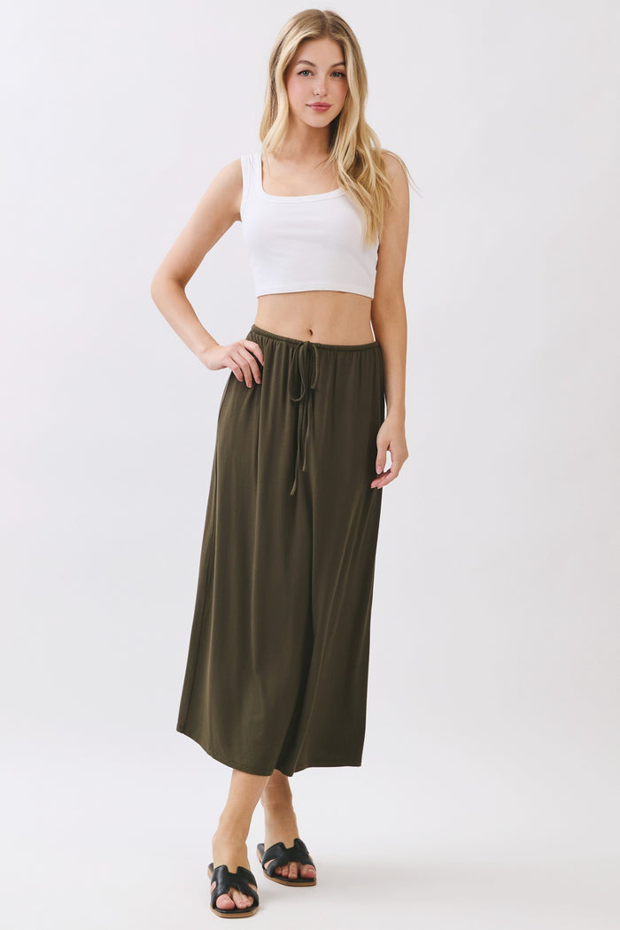 woman wearing an olive green maxi skirt with an elastic waistband and drawstring, paired with a white cropped tank top