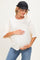 woman wearing a cream maternity top and blue jeans, holding her baby bump, and wearing a black cap