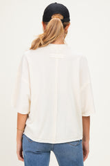 woman wearing a cream-colored maternity top with a relaxed fit and back seam detail, styled with a black cap