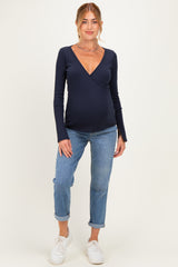 woman wearing a navy blue long sleeve maternity wrap top and light blue rolled jeans, showing her baby bump