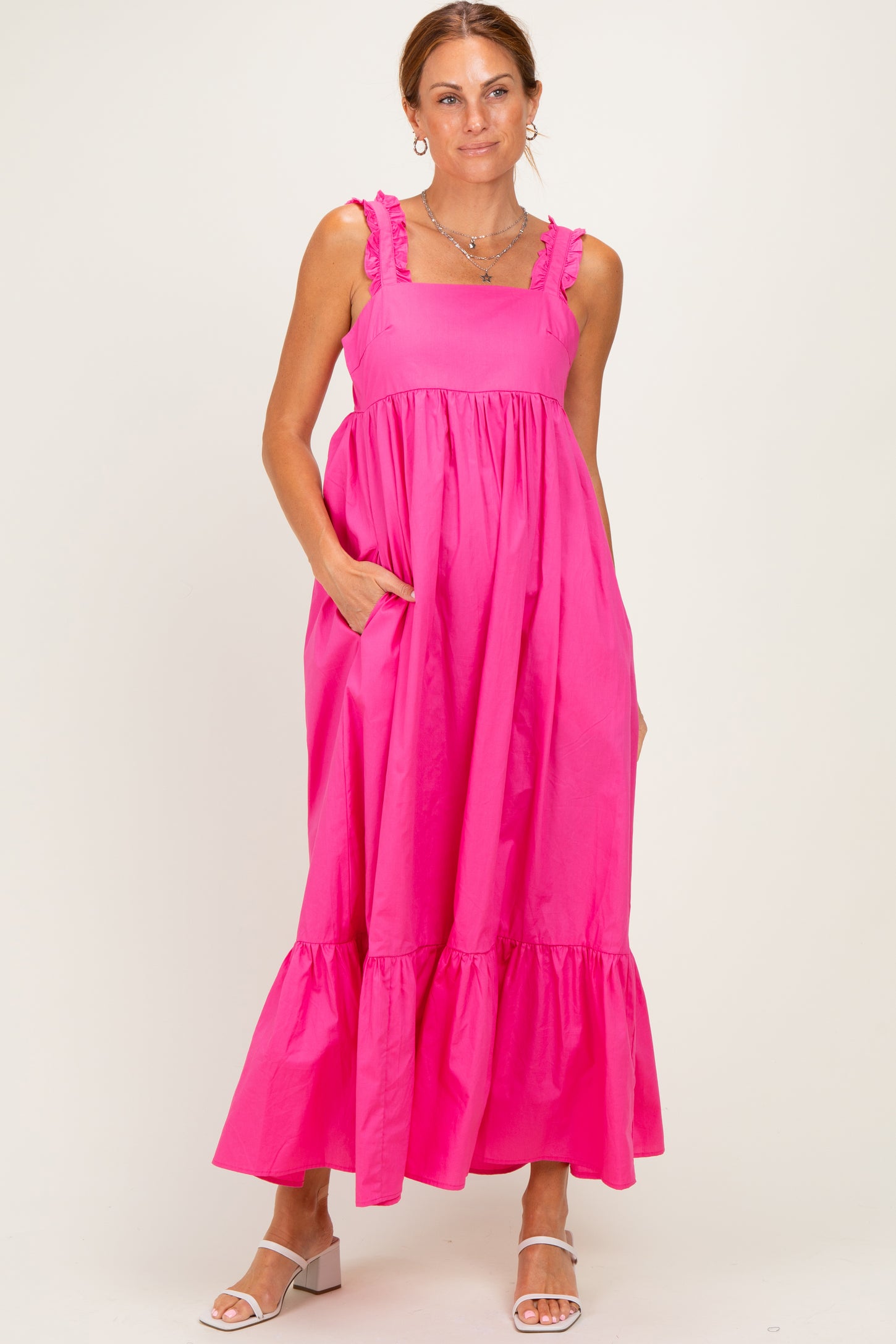 woman wearing a pink maxi dress with ruffle straps and a tiered hem, standing with hands in pockets