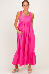 woman wearing a pink maxi dress with ruffle straps and a tiered hem, standing with hands in pockets