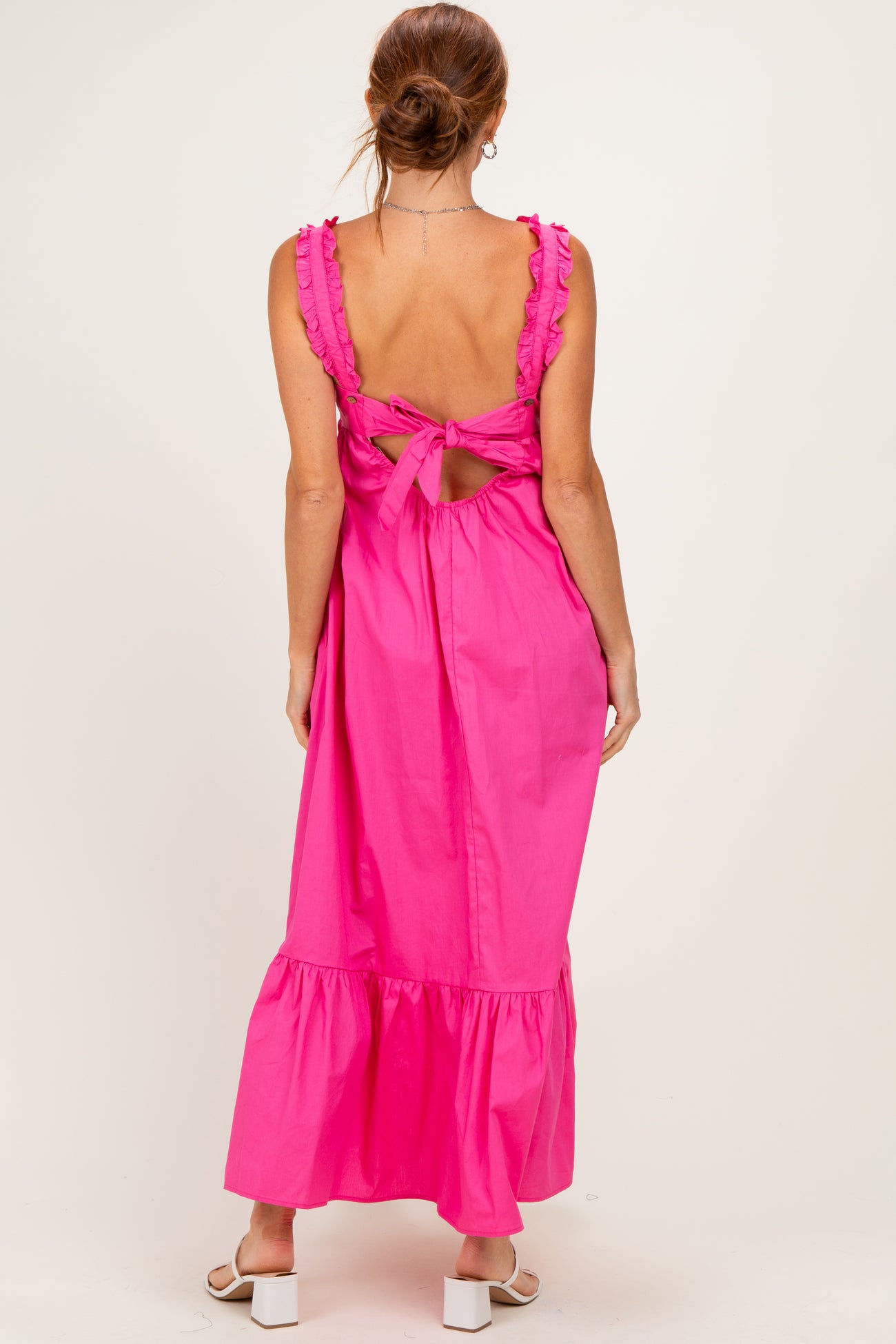 woman wearing a hot pink backless maxi dress with ruffled straps and a flared hem